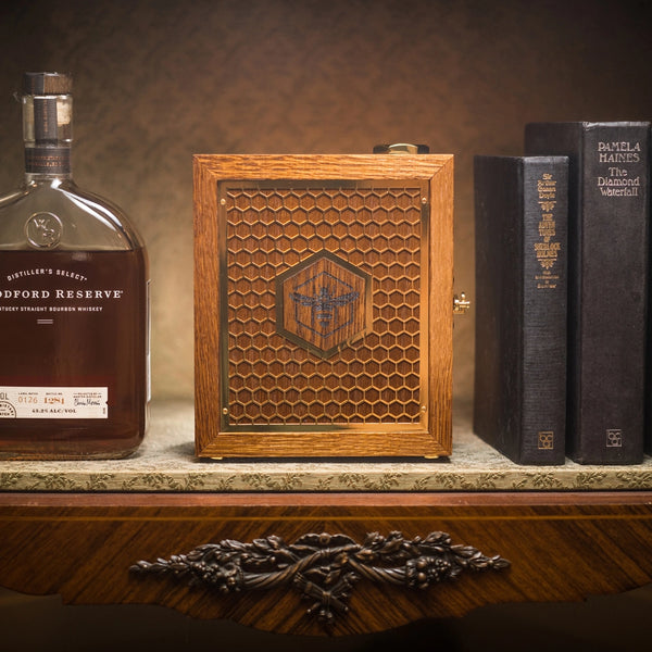 whiskey bottle, manuka honey presentation case, and books placed on top of a table