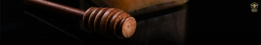 Close-up of a wooden honey dipper beside a jar of honey on a dark background, representing Best Manuka Honey.
