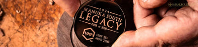 Hands holding a Manuka South Legacy honey jar on natural soil surface.
