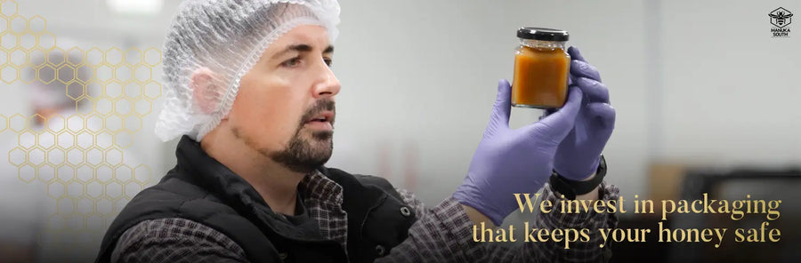 A man wearing a hairnet and gloves in a food production setting carefully inspects a small jar of Manuka honey. Text overlay reads: "We invest in packaging that keeps your honey safe".
