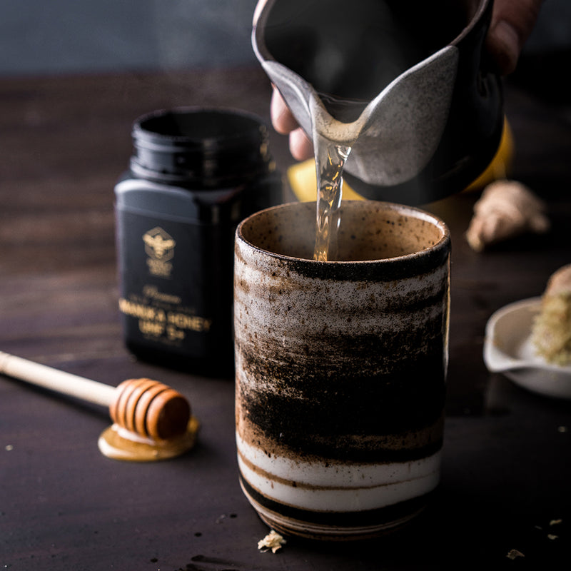 manuka honey on dibber behind hot drink of tea
