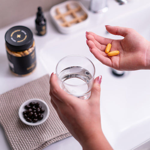 woman holding yellow capsules on her right hand and a glass of water on the left